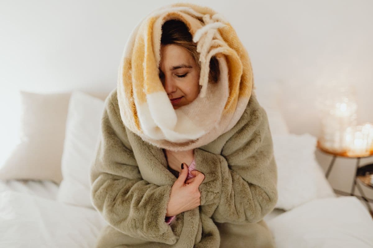 Person feeling cold indoors despite thermostat set to a warm temperature.