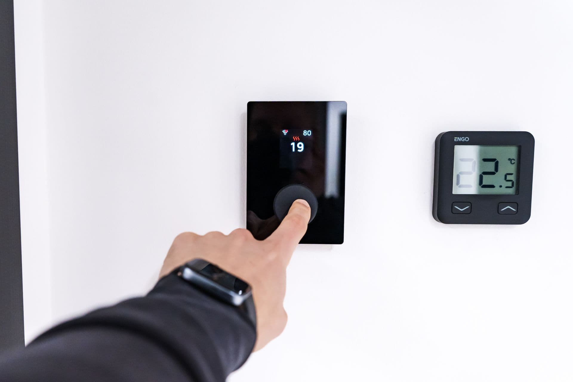 A hand adjusting a digital zone-control thermostat on a wall