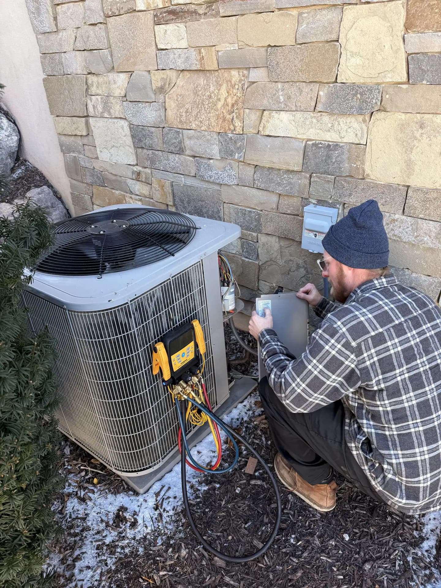 A technician servicing an AC condenser at a stone-clad home