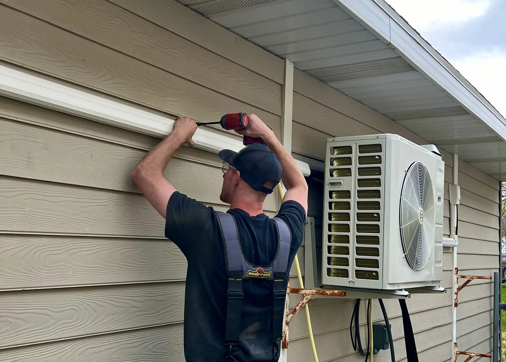 Technician mounting a ductless mini-split condenser to a home exterior
