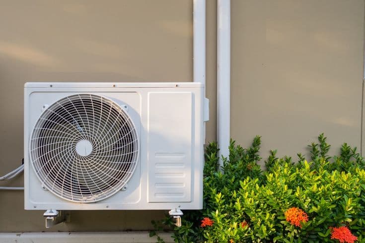 Outdoor ductless mini-split condenser unit installed near garden shrubs at a Utah home.