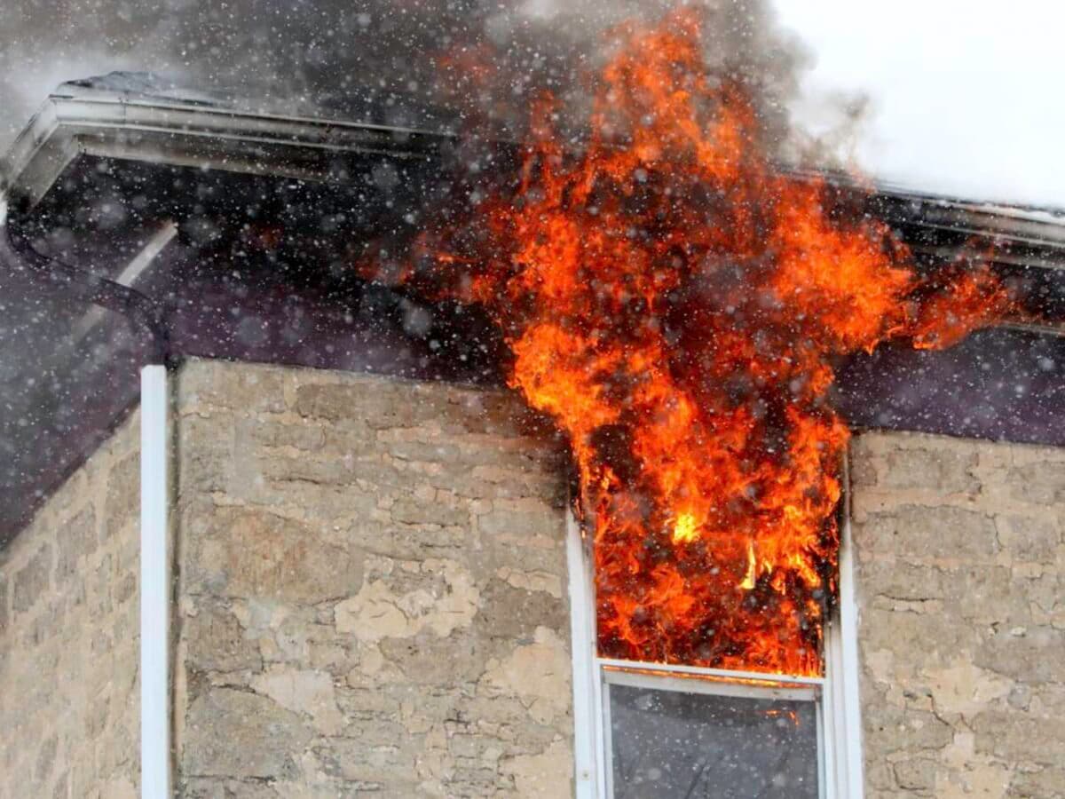 House fire erupting from an upper floor window on a hot day, showing the risks of neglected AC units or electrical hazards during summer.
