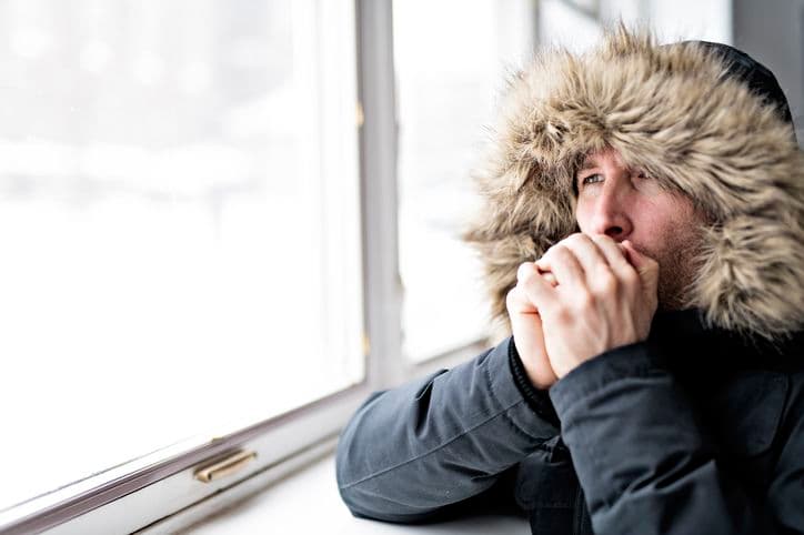 Person feeling cold indoors despite thermostat set to a warm temperature.