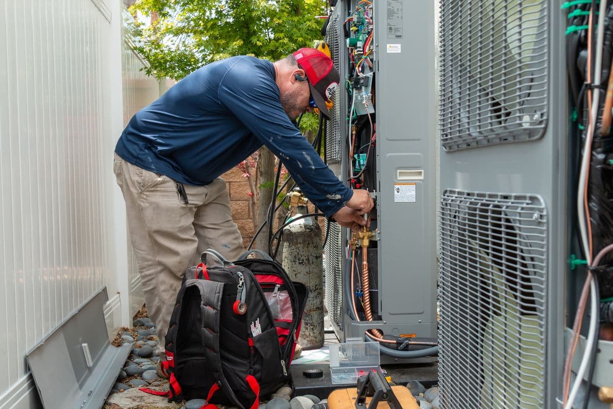 HVAC technician servicing an outdoor air conditioning unit during a spring AC maintenance inspection.